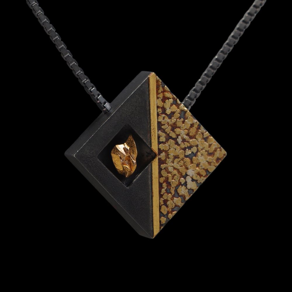 A black and gold square shaped necklace with a golden animal on it.