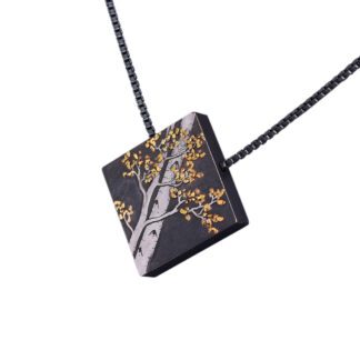 A square black and gold necklace with an image of a tree.