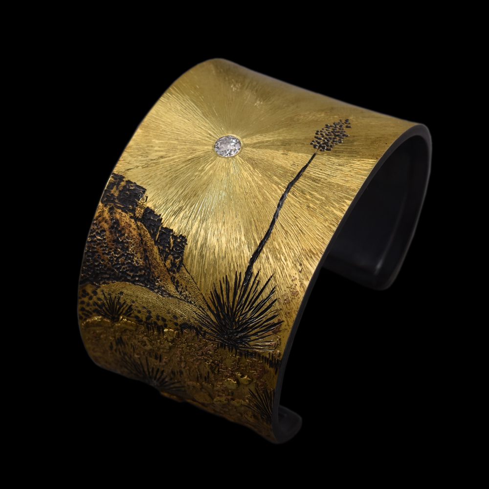 A gold cuff bracelet with an image of desert.