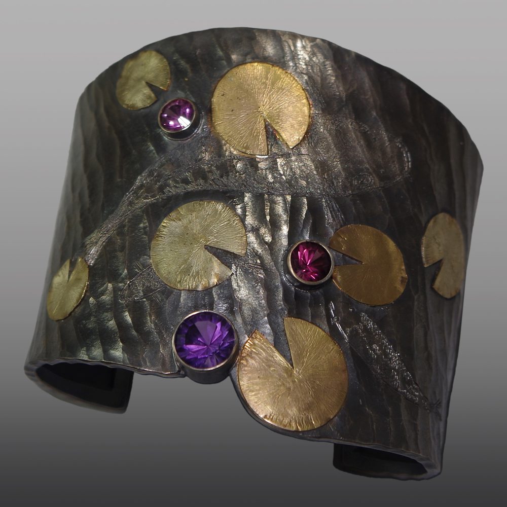 A metal cuff with gold and purple stones.