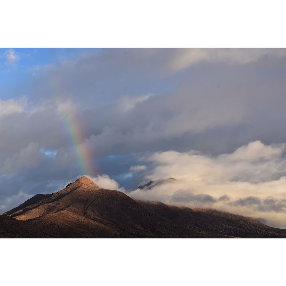 A rainbow is seen in the sky above a mountain.