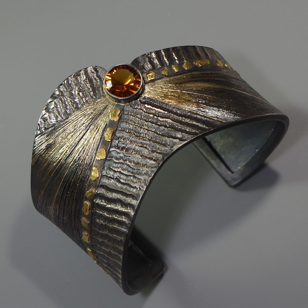 A metal bracelet with a yellow stone on it.