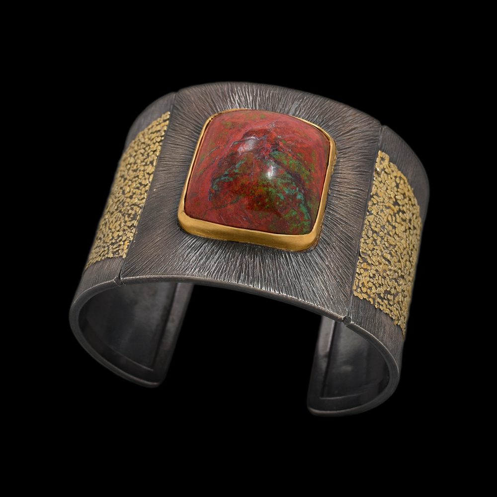 A cuff bracelet with gold and red stone.