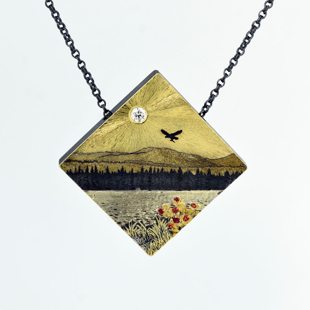 A necklace with a picture of a bird flying over the mountains.