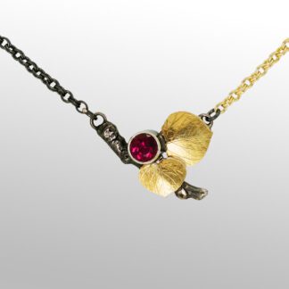 A necklace with a red stone and gold leaves.